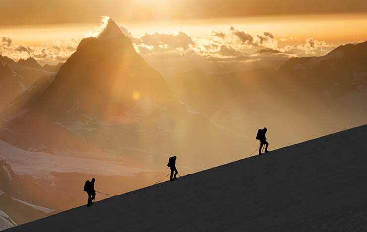 Climbers on a snowy ridge at sunrise ascending the Monte Rosa  On the background the Matterhorn 